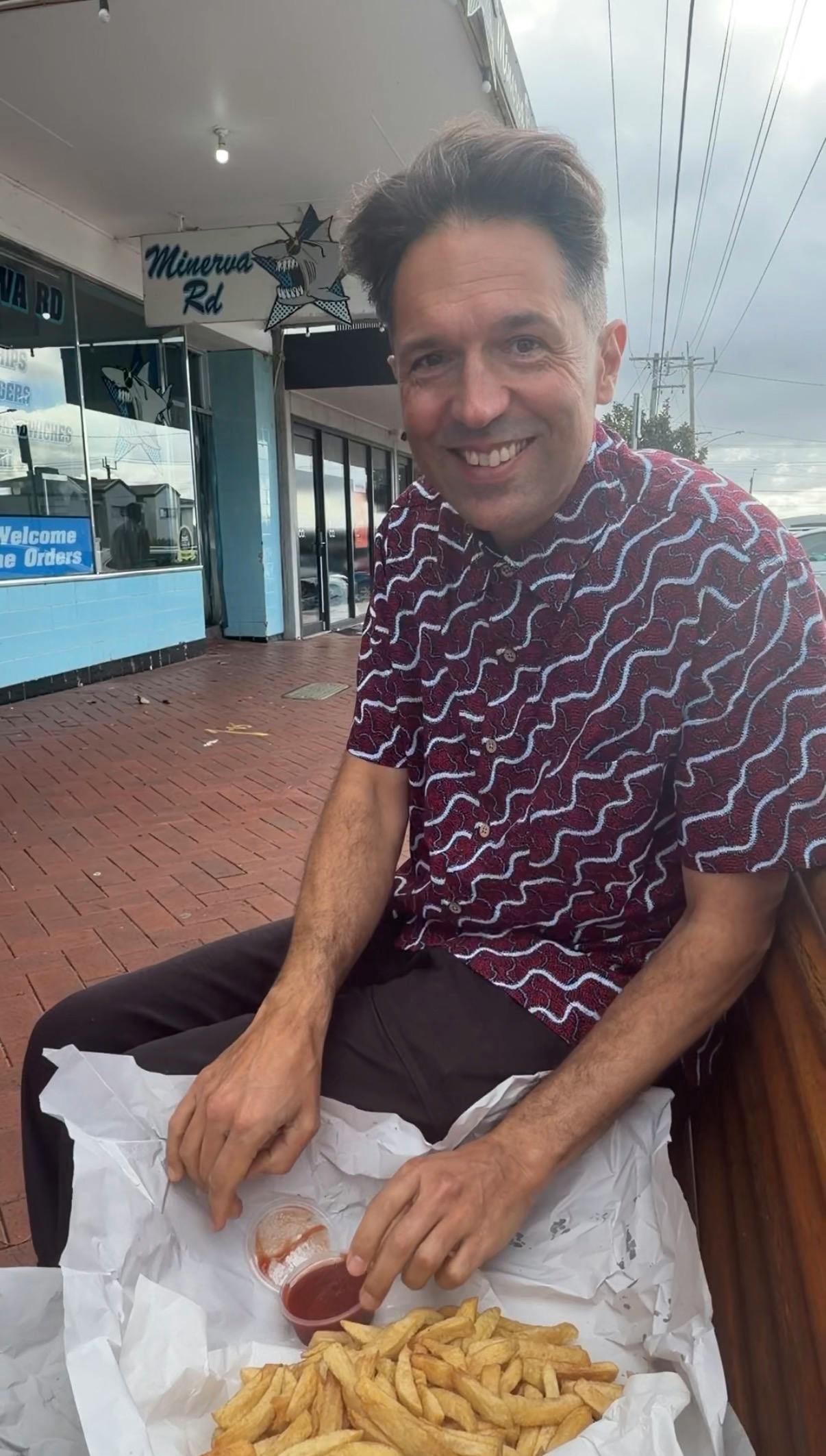 Ben Shewry eating a takeaway pack of hot chips on a park bench from Minverva Rd Fish & Chips